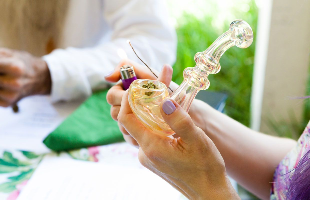A clear yellow pink pipe filled with bud is about to be lit by a hemp wick.