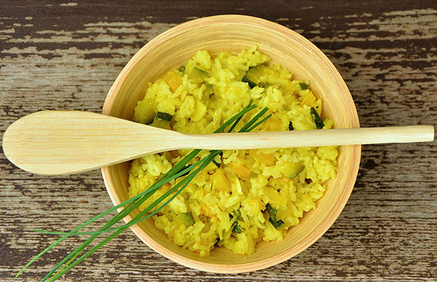 Bright yellow Jack Herer infused butternut squash risotto sits in a yelloware bowl, with a wooden spoon sitting atop.